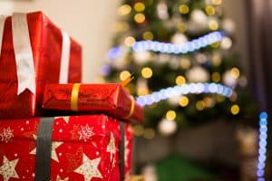 red christmas packages stacked to the left with a christmas tree with lights strung behind