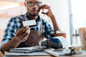 man sitting at a desk on the phone holding up a credit card with paper work at desk