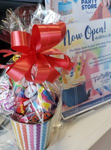 small gift basket with goodies and treats with a red bow on top and a sign next to it that says now open