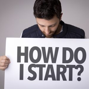 man looking down at a sign he is holding that prints "how do I start?"