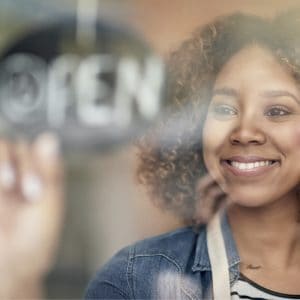 close up of woman employee smiling and flipping over the open sign on a window